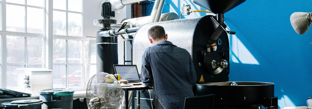 Ein Mann arbeitet an einem Laptop vor einer großen Industriemaschine in einer modern ausgestatteten Fabrikumgebung.